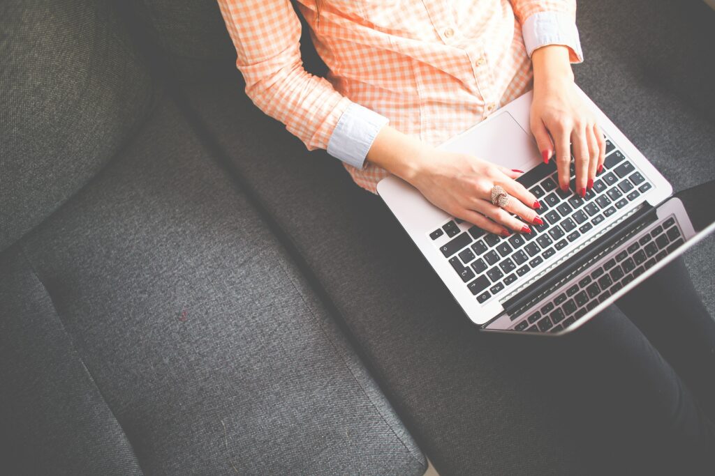 Widoczna osoba pracująca na laptopie, trzymająca go na kolanach i mająca ręce na klawiaturze